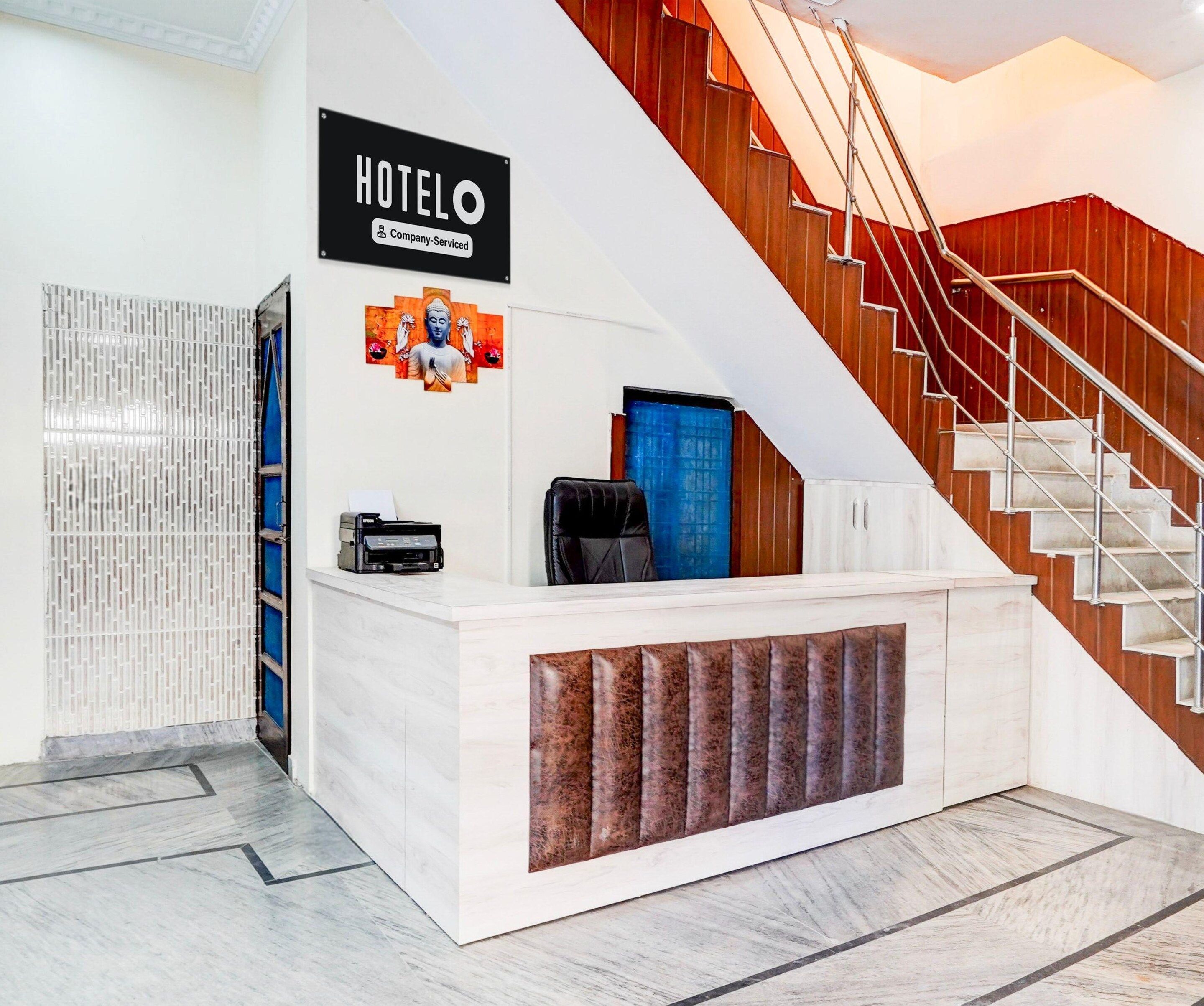 A hotel reception desk with a sign reading 'HOTELO Company-Serviced', a printer, and a blue door.