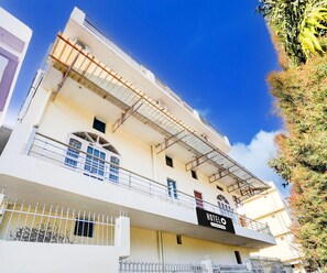 A multi-story hotel with a balcony on the ground floor, a sign indicating it is a company-serviced hotel, and a clear blue sky in the background. - Saver Double Hotel White Retreat Inn (Vikasnagar)