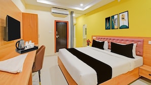A hotel room with a bed, bedside table, chair, desk with a kettle and cups, a TV, and artwork on the wall. - Townhouse Mindspace Road Gachibowli (Hyderabad)