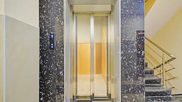 An elevator with a digital display, marble walls, and a metal staircase.
