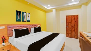 A hotel room with a bed, a wooden nightstand, a desk, and a door.