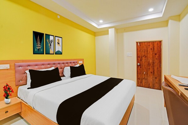 A hotel room with a bed, a wooden nightstand, a desk, and a door.