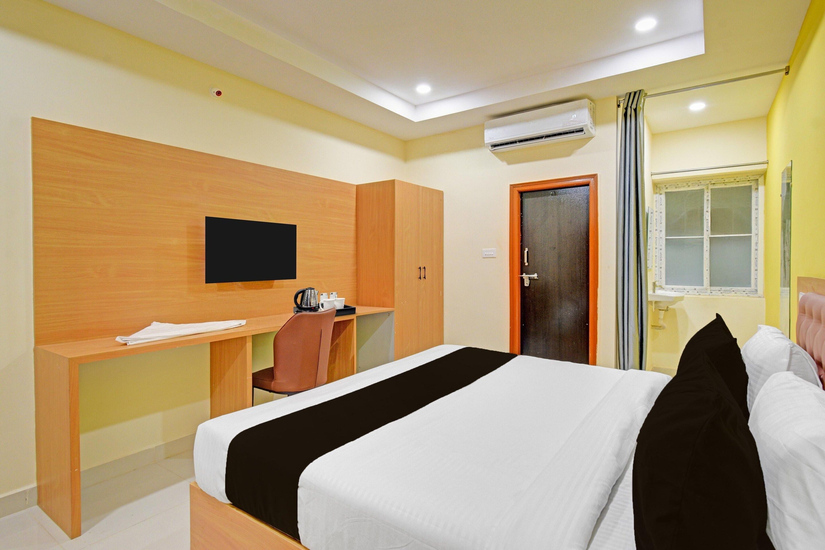 A hotel room with a bed, a desk, a chair, a television, and an air conditioning unit.