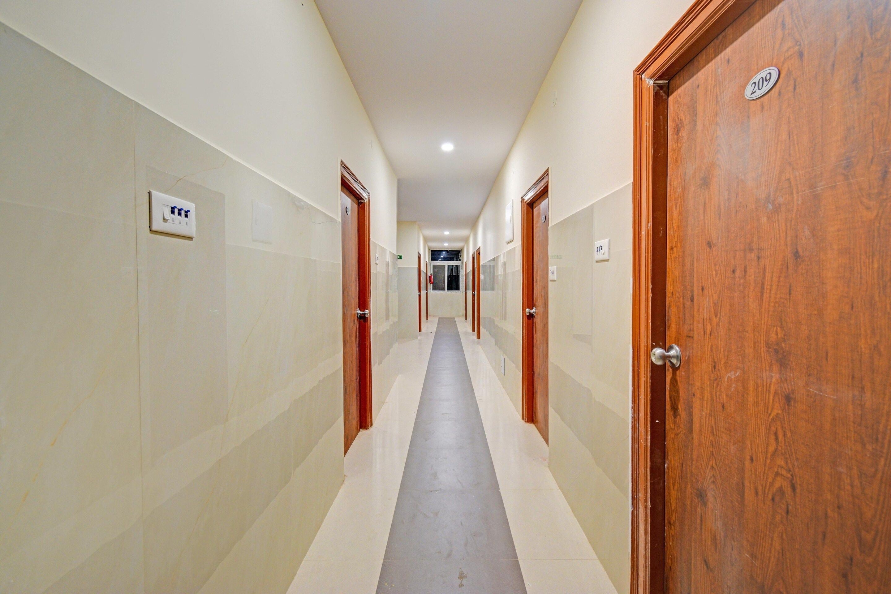 A corridor with doors on both sides, a tiled floor, and a ceiling with recessed lighting.