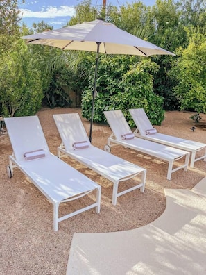 Three white lounge chairs with cushions, an umbrella, and a gravel area. - Modern Scottsdale|Salt Pool + Hot Tub + Fire Pit (Scottsdale)