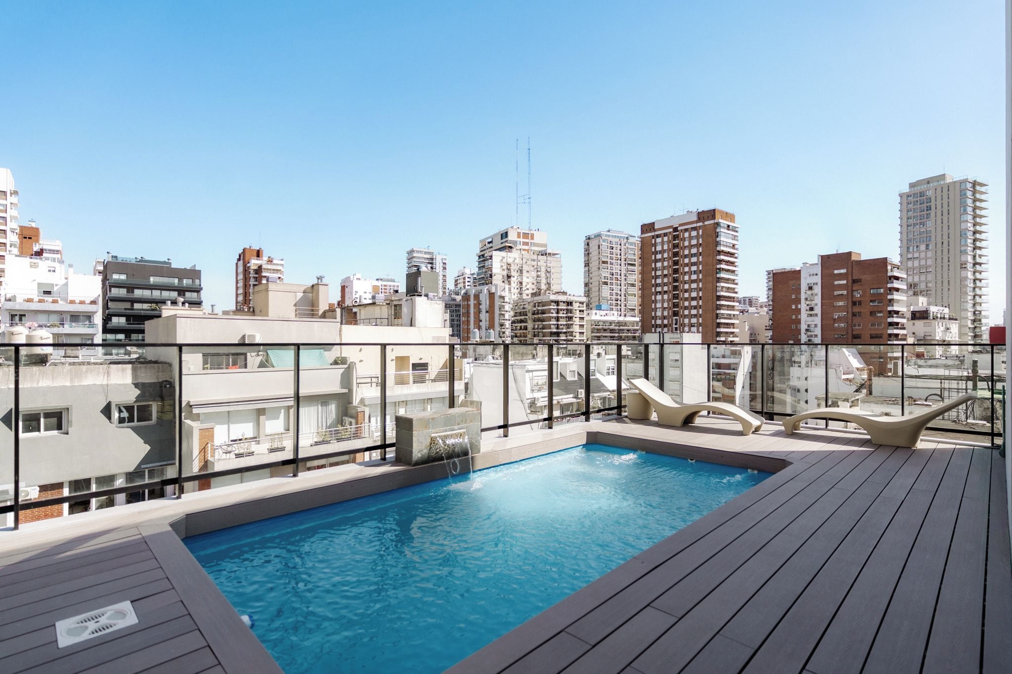 Una piscina en la azotea con vistas a un paisaje urbano, rodeada de edificios modernos.
