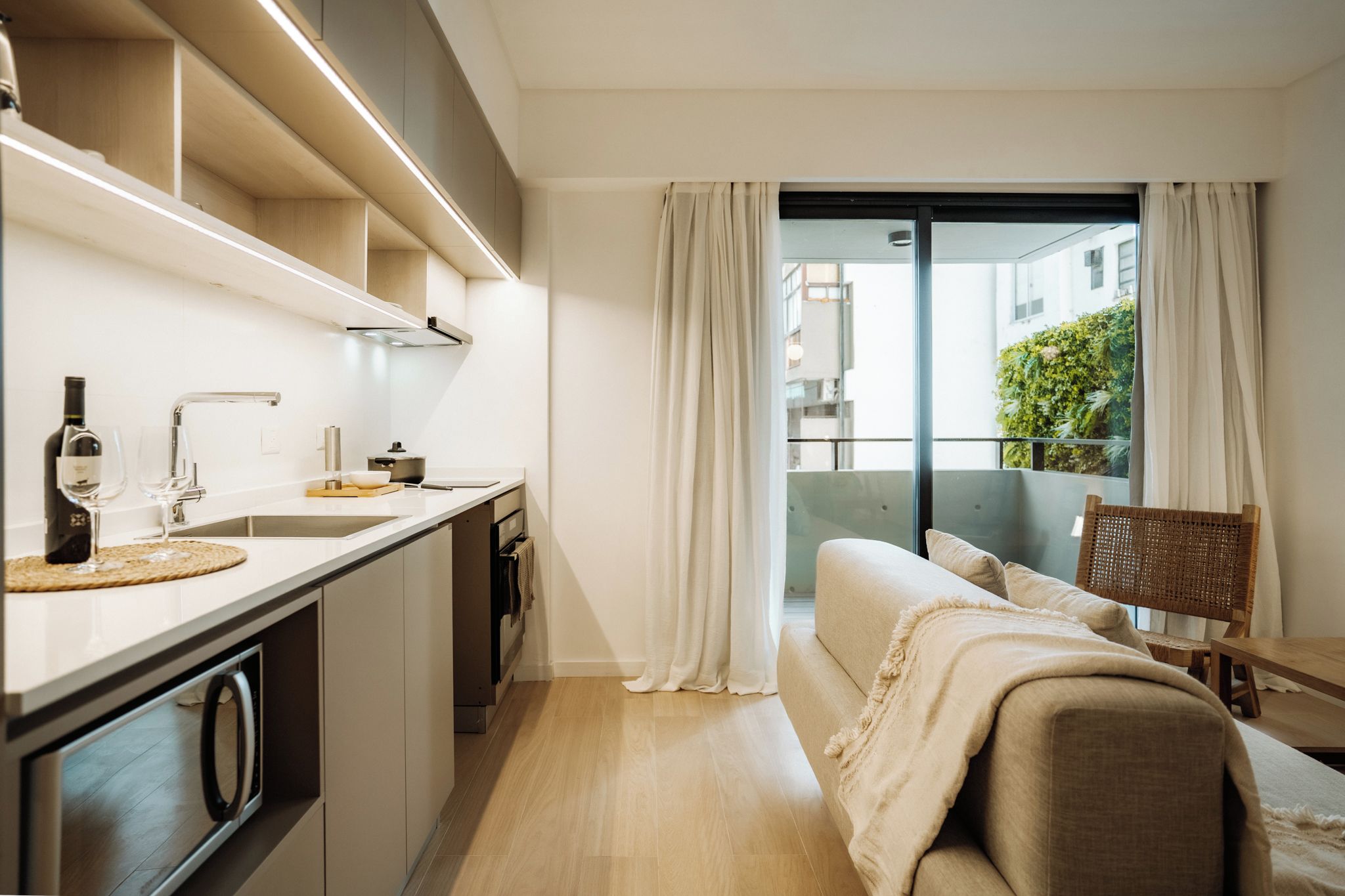 A modern kitchen with a built-in oven, a sink, and a dining area with a sofa and a chair.