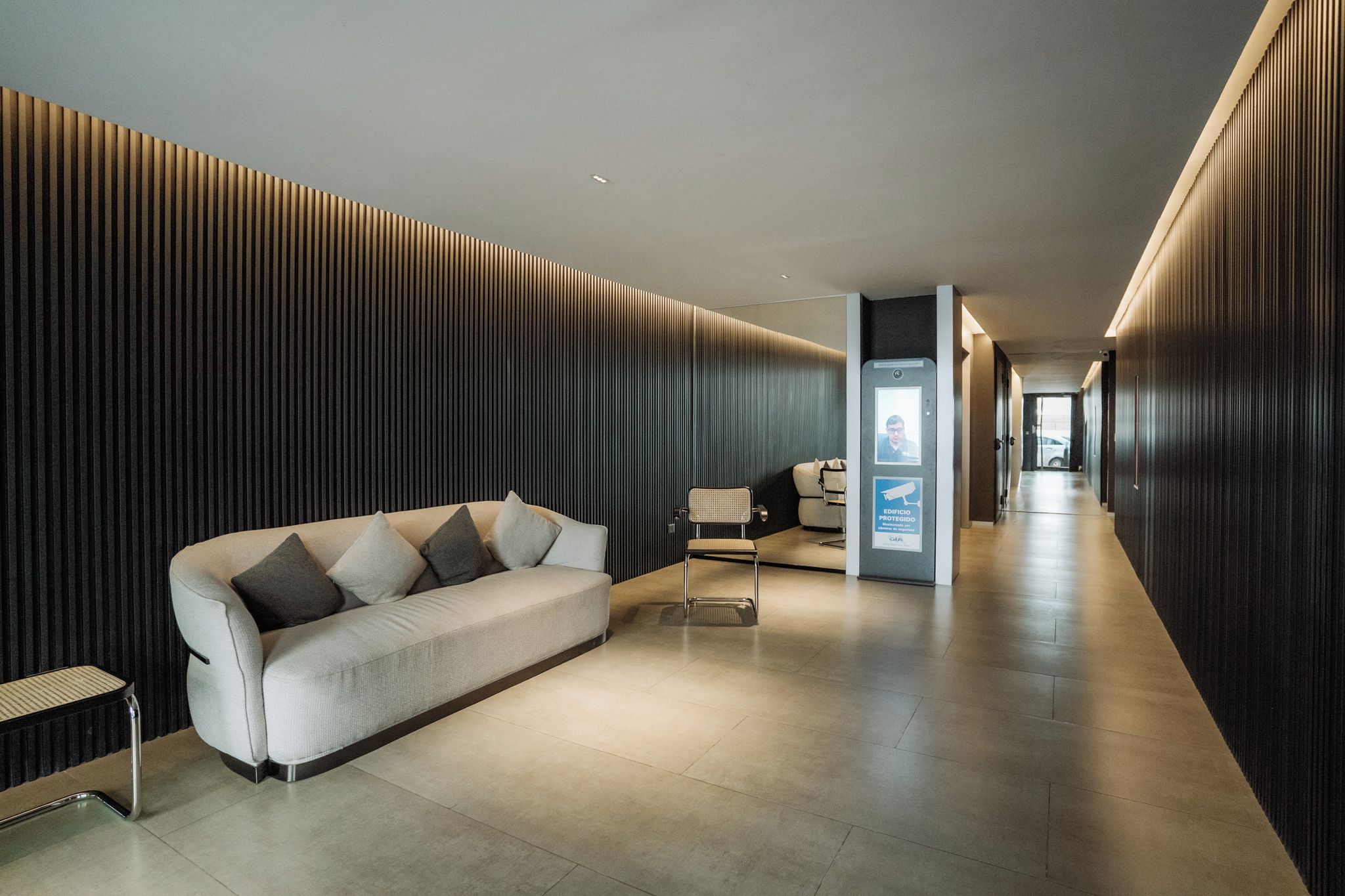 A modern hallway with a sofa, a chair, and a security kiosk.