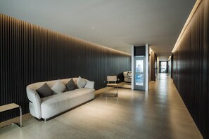 A modern hallway with a sofa, a chair, and a security kiosk. - Hestia at Casa Solado (Buenos Aires)