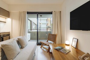A modern hotel room with a sofa, a wooden chair, a table with a magazine, a wall-mounted TV, and a view of the outside balcony. - Hestia at Casa Solado (Buenos Aires)