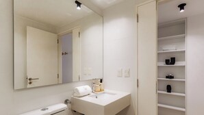 Et moderne badeværelse med en hvid vask, et spejl, et håndklæde og en hylde med toiletartikler.