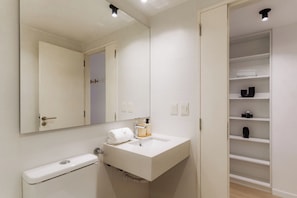 A modern bathroom with a white sink, a mirror, a towel, and a shelf with toiletries. - Hestia at Casa Solado (Buenos Aires)