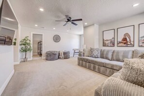 A living room with a sofa, ottomans, a ceiling fan, a clock, and framed pictures on the wall. - Heated Pool, Lazy River, Hot Tub, Pickleball, 5 EnSuites (Washington)