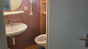 A bathroom with a wooden ceiling, a round mirror, a white sink, a toilet, and a blue and black patterned rug. - Charming garden cottage with open gallery in Erlach (Erlach)
