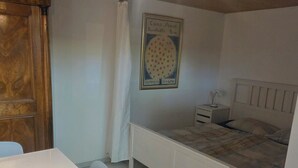 A bedroom with a bed, a bedside table, a nightstand, a white desk, and a wooden wardrobe. - Charming garden cottage with open gallery in Erlach (Erlach)