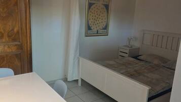 Un dormitorio con cama, mesita de noche, escritorio blanco y armario de madera.