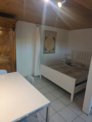 A bedroom with a bed, a bedside table, a nightstand, a white desk, and a wooden wardrobe. - Charming garden cottage with open gallery in Erlach (Erlach)