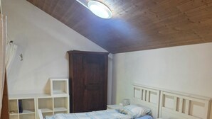 A bedroom with a wooden ceiling, a bed with a white headboard, a bedside table, and a wardrobe. - Charming garden cottage with open gallery in Erlach (Erlach)
