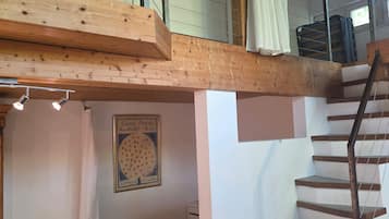 Un dormitorio con techo de madera, una cama, una escalera y un ventanal.