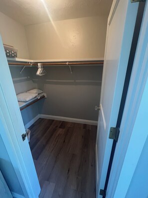 A small, enclosed closet with a wooden rod for hanging clothes, a bench with pillows, and a plastic bin on the floor. - Amazing Ranch Home located on a 155 acre ranch 10 minutes from downtown Paso. (Paso Robles)