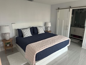 Ein Schlafzimmer mit einem Bett, zwei Nachttischen, einem Schminktisch, einer Lampe, einer Kommode und einer Schiebetür zu einem Badezimmer.