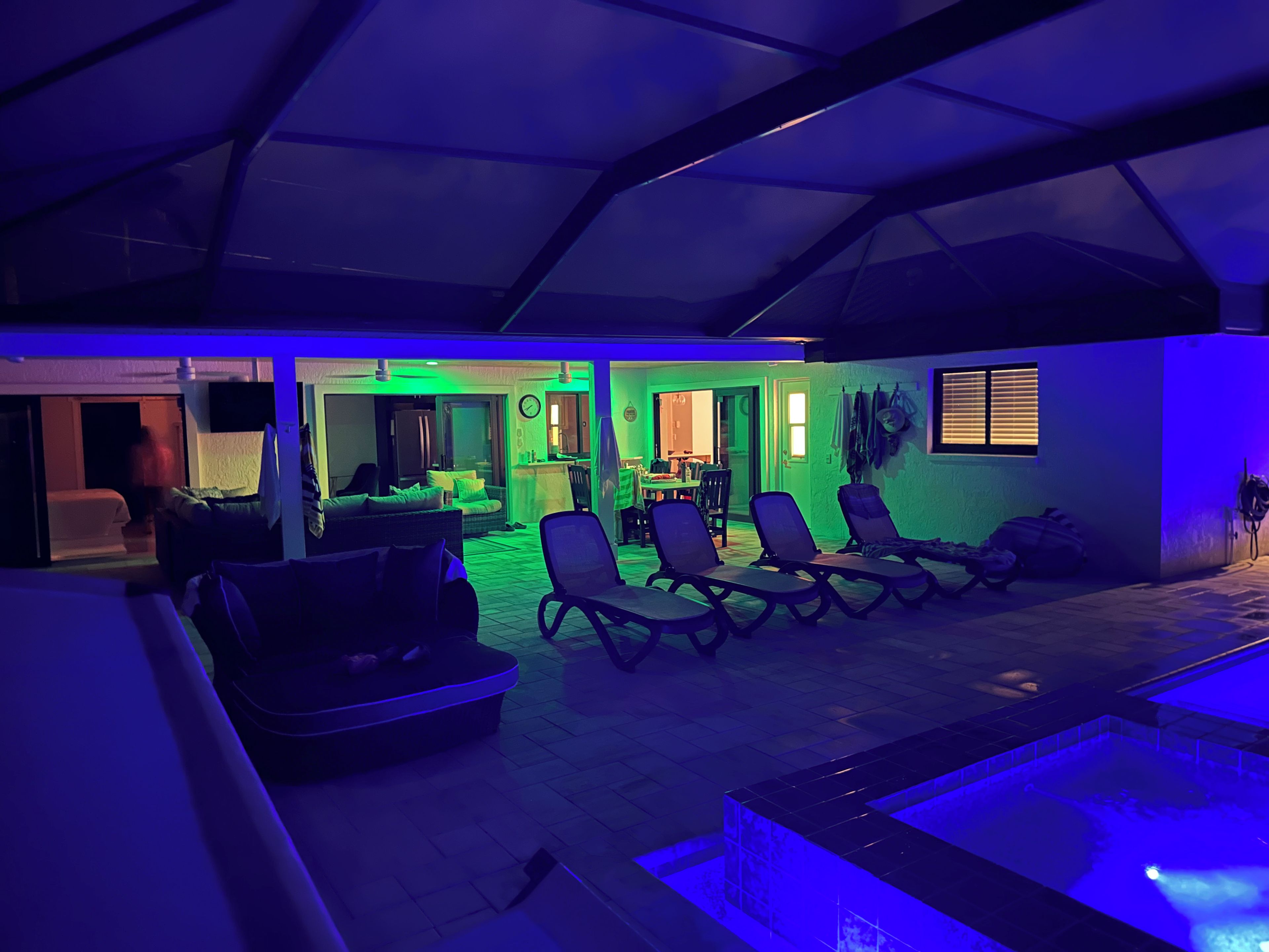 A room with a pool, lounge chairs, and a dining area.