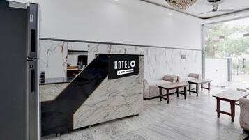 Ein Hotelrezeptionsschalter mit Marmordesign, einem Schild, das OYO ausweist, und einer Sitzecke inklusive Sofa und Tischen.