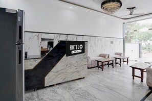 A hotel reception desk with a marble design, a sign indicating it is serviced by OYO, and a seating area with a sofa and tables. - Deluxe Xponest Hotel (Greater Noida)