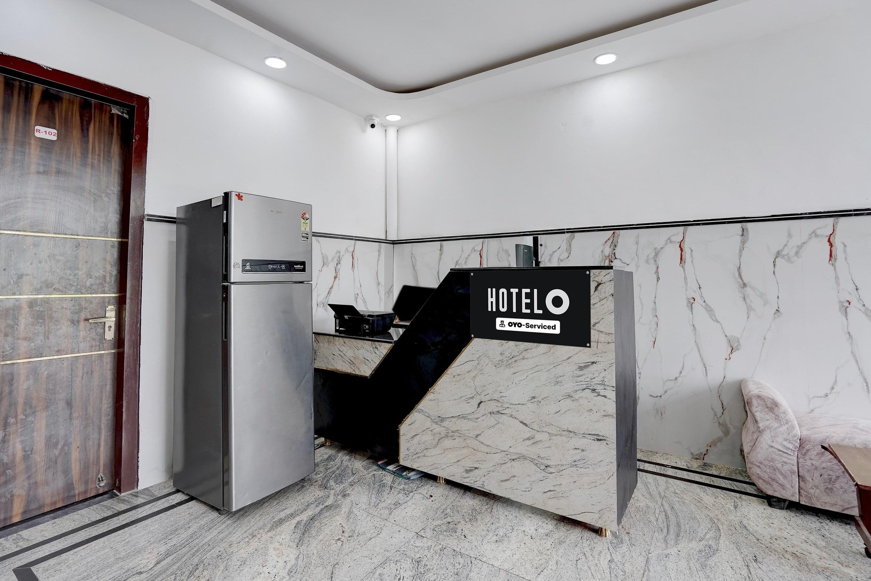 Zona de recepción de hotel con pared de mármol, mostrador de recepción, refrigerador y una puerta.
