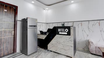 Zona de recepción de hotel con pared de mármol, mostrador de recepción, refrigerador y una puerta.