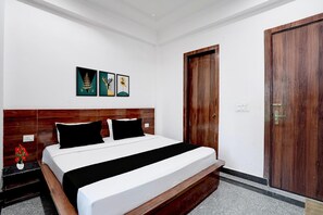 A hotel room with a wooden headboard, a bed with white and black bedding, and a door with a wooden panel. - Deluxe Xponest Hotel (Greater Noida)