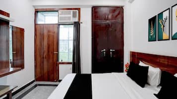 Habitación de hotel con cama, escritorio, aire acondicionado, armario y ventana con cortinas.