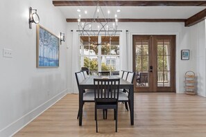 A dining area with a table and chairs, a chandelier, and a view through large windows.
