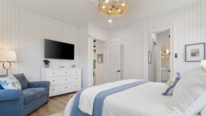 Un dormitorio con cama, cómoda, televisor y puerta que da a un baño.