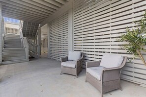 A covered outdoor area with two wicker chairs and a staircase leading to an upper level.