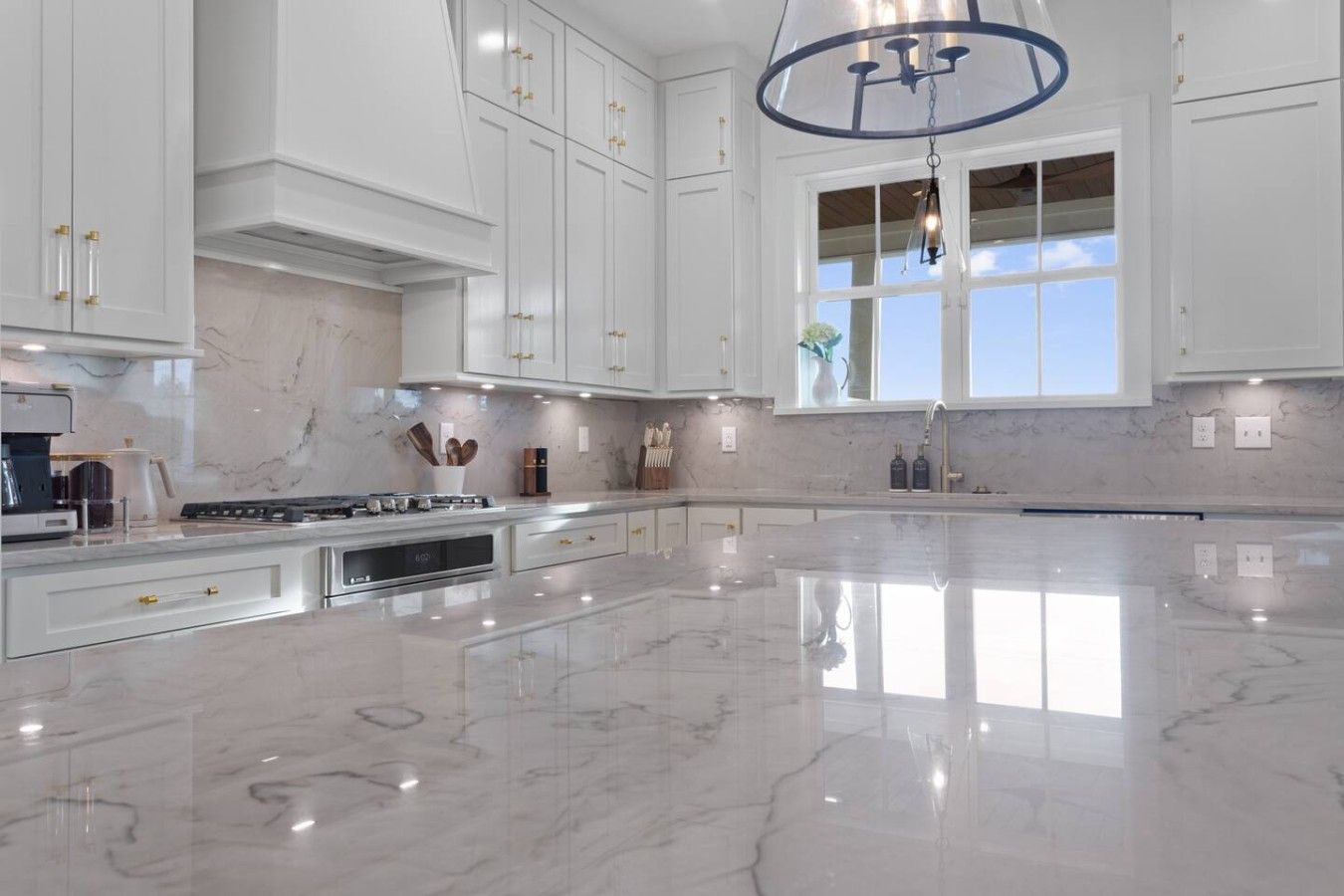 A spacious kitchen with white cabinetry, a marble countertop, and a large window.