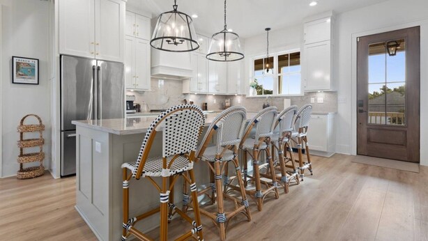Una cocina moderna con armarios blancos, un refrigerador de acero inoxidable y una isla central con taburetes de bar.