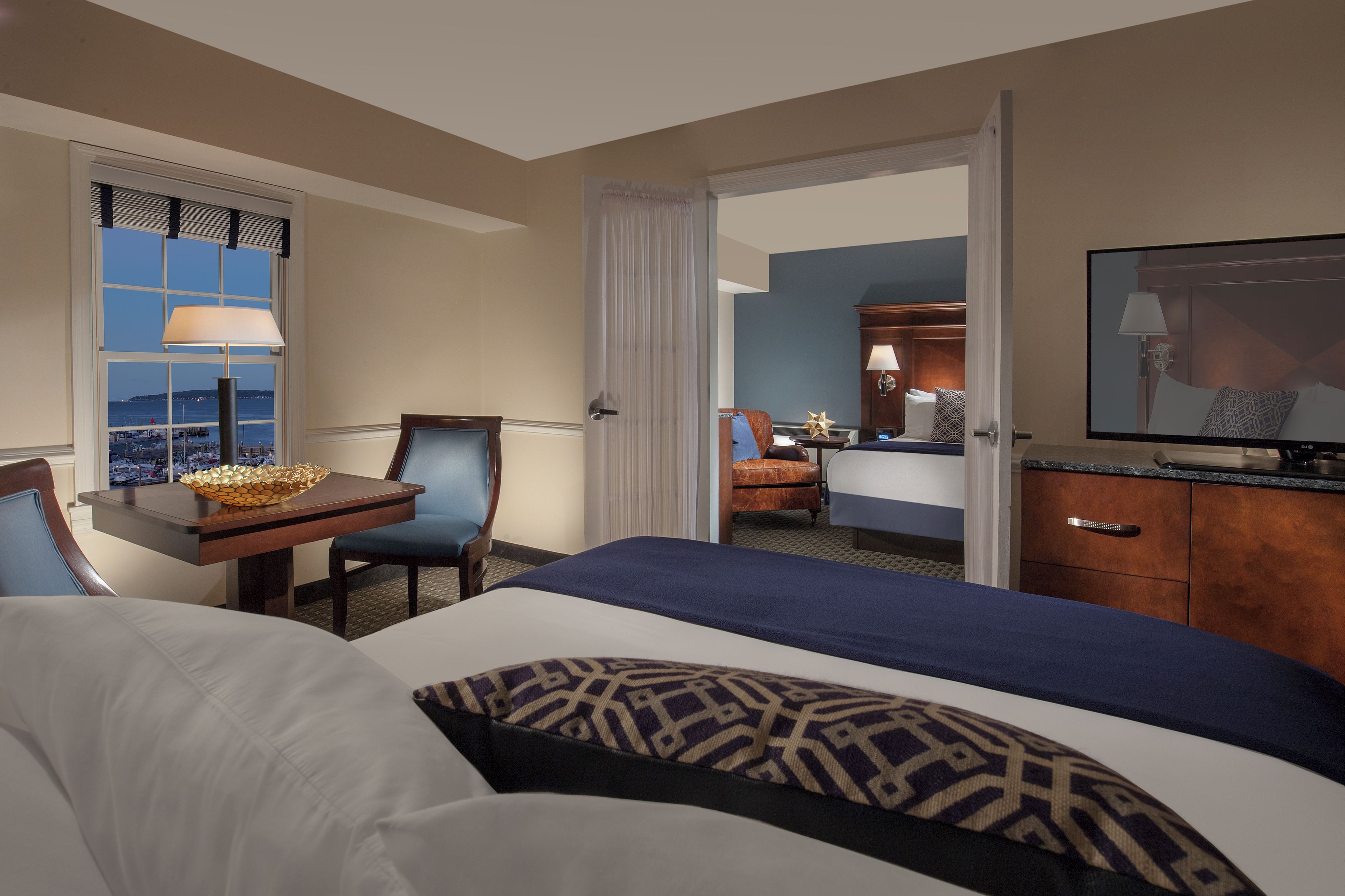 A hotel room with a bed, a desk with a lamp, a chair, and a television.