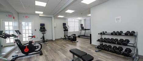 A gym with exercise equipment, a bench, and a rack of dumbbells.