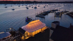A marina at dusk with multiple boats docked, a covered seating area, and a view of the water. - Bristol Harbor Inn (Bristol)