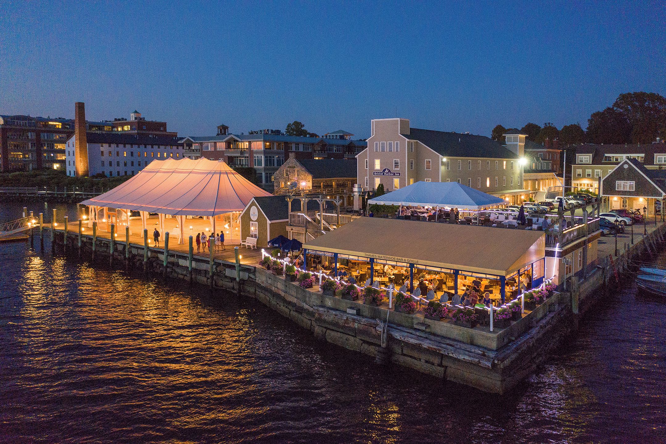 A waterfront restaurant with outdoor seating, a covered area, and a dock extending into the water.