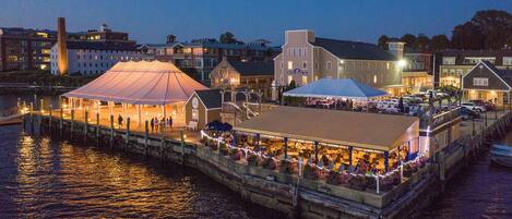 A waterfront restaurant with outdoor seating, a covered area, and a dock extending into the water.