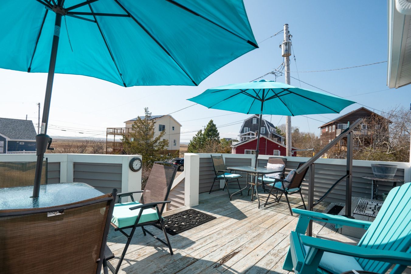 An outdoor patio with a wooden deck, outdoor seating, and a view of houses in the background.