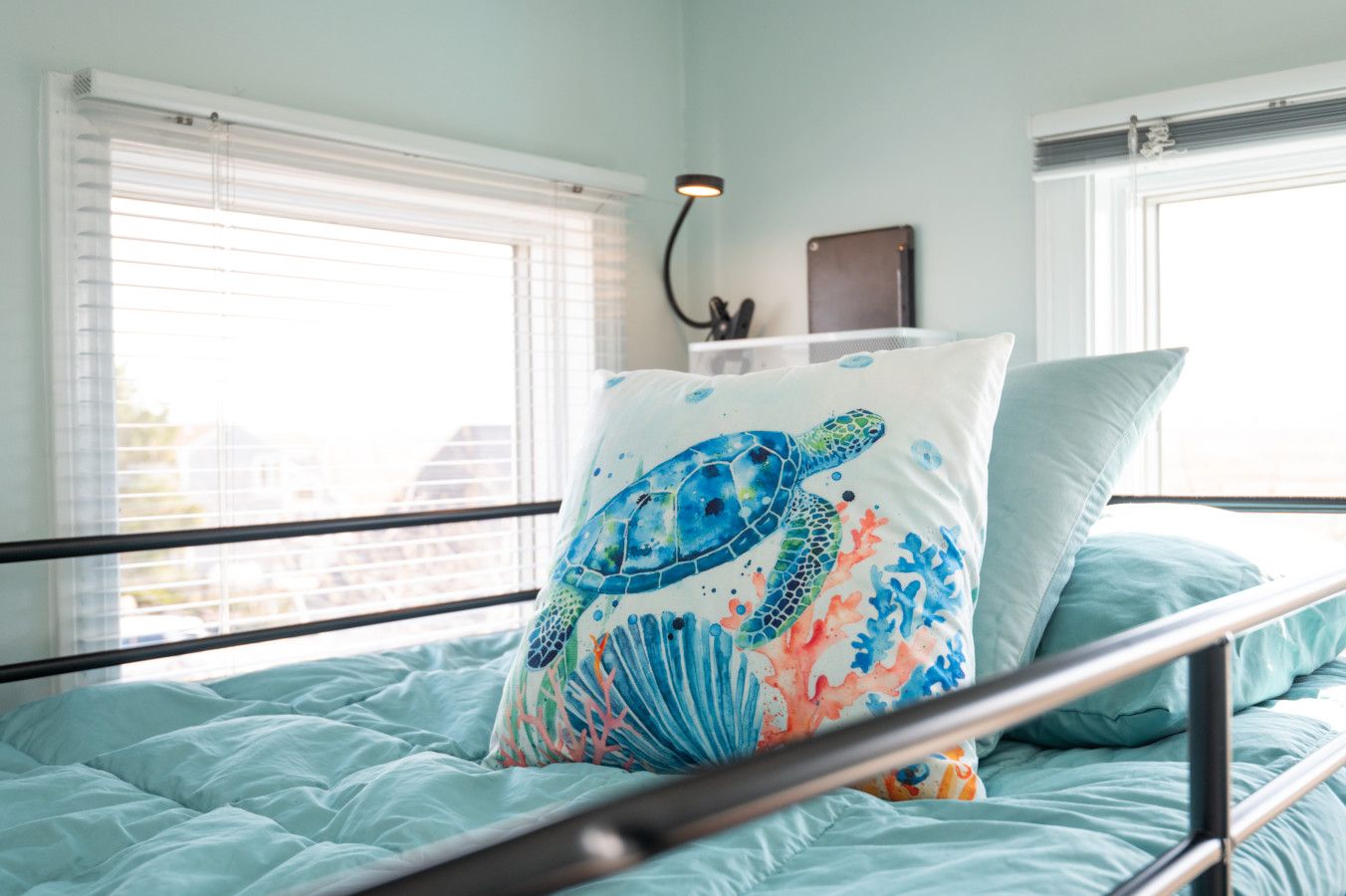Een bed met een blauwe spreideken, een kussen met het ontwerp van een zeeschildpad en een bedlampje.