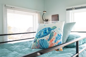 A bed with a blue bedspread, a pillow with a sea turtle design, and a bedside lamp.