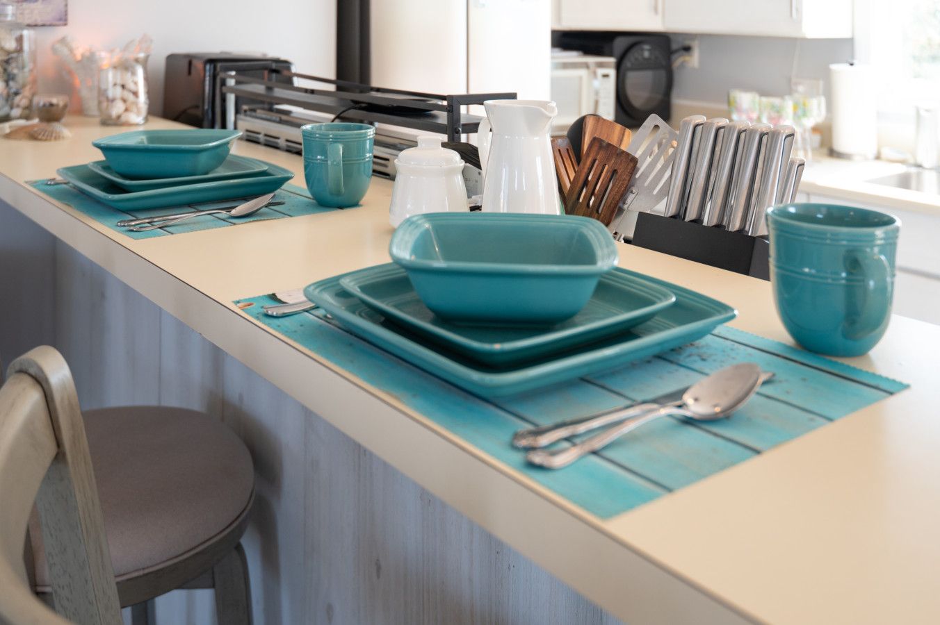 Un plan de travail de cuisine avec de la vaisselle de couleur turquoise, un pichet blanc et un bloc à couteaux.