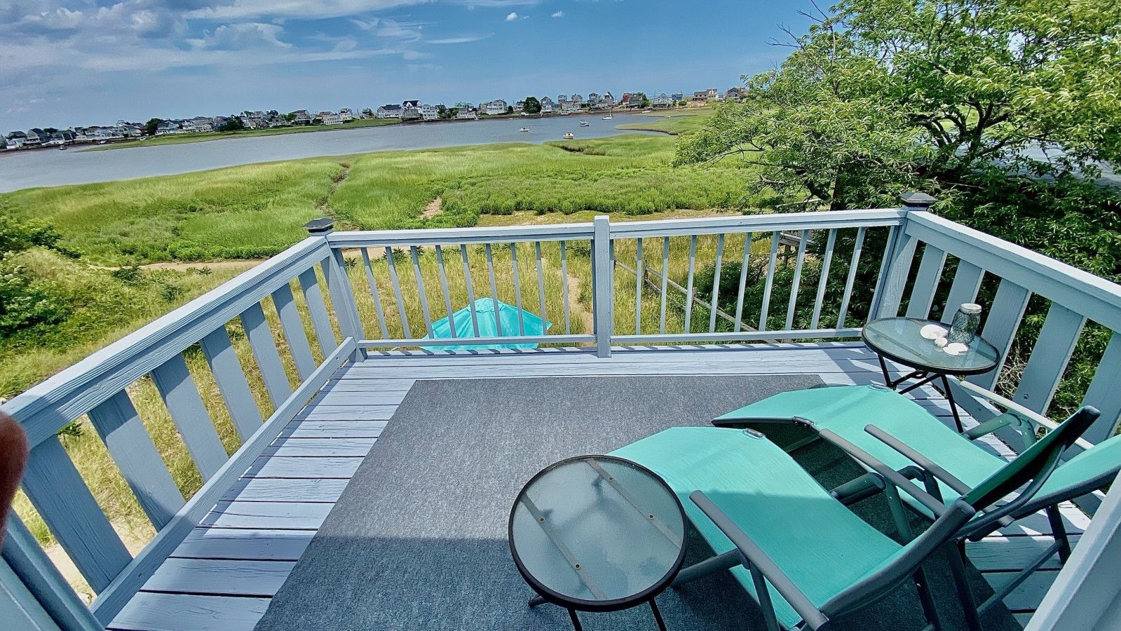 Une terrasse offrant une vue sur un plan d’eau, une zone herbeuse et une rangée de maisons au loin.