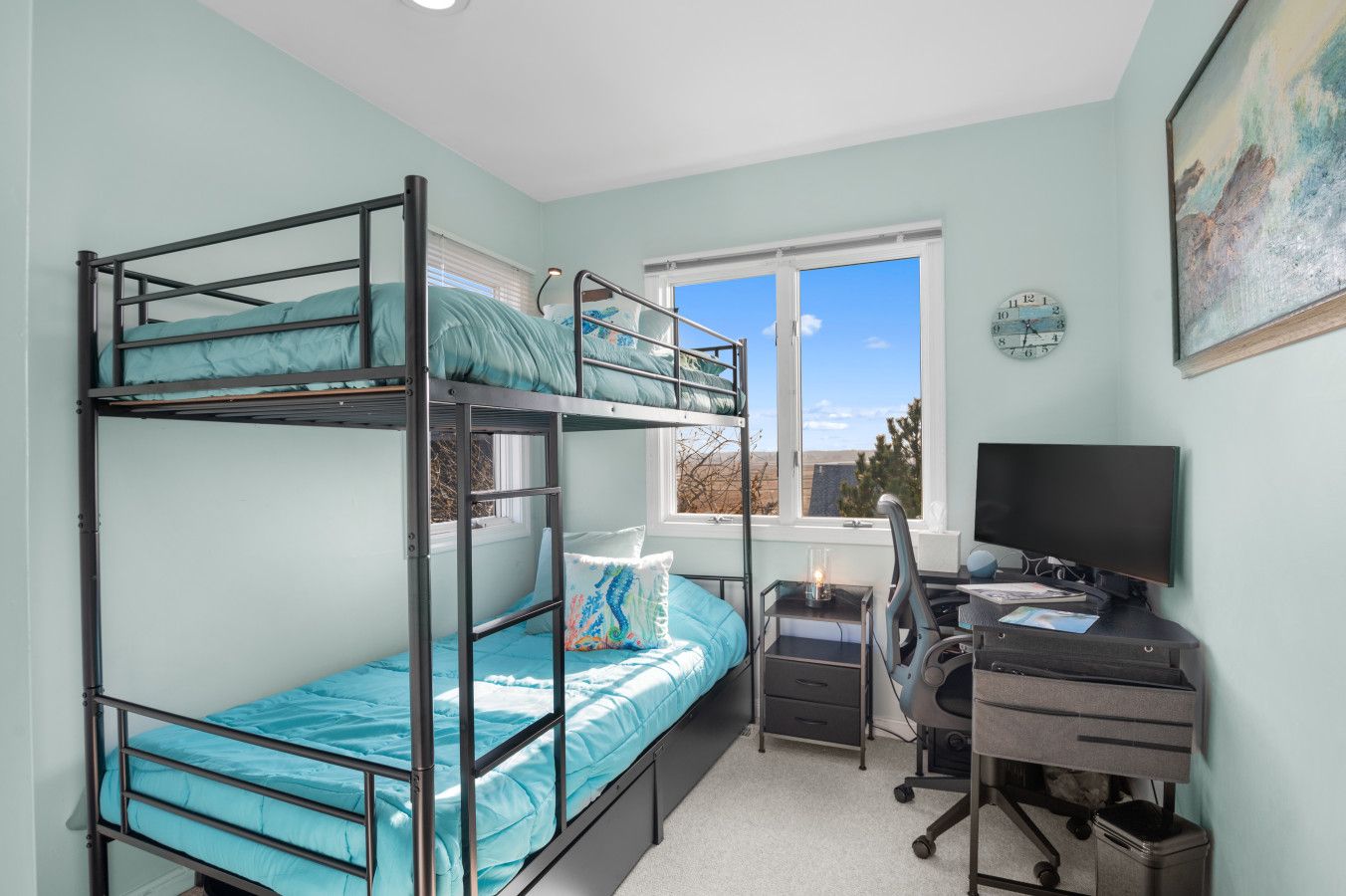 A dormitory room with bunk beds, a desk, a chair, a computer, and a window with a view.