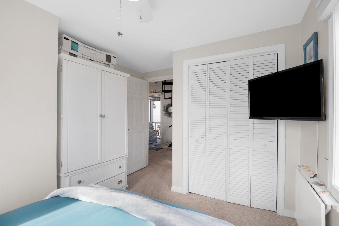 A bedroom with a bed, a wardrobe, a television, and a hallway leading to another room.