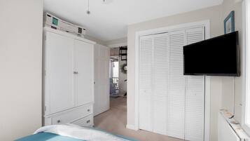 A bedroom with a bed, a wardrobe, a television, and a hallway leading to another room.